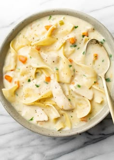 a bowl filled with chicken noodle soup on top of a white marble countertop