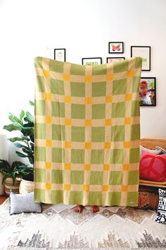 a green and yellow checkered blanket sitting on top of a bed next to a potted plant