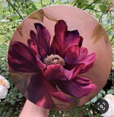 a person's hand holding up a purple flower on top of a wooden plate