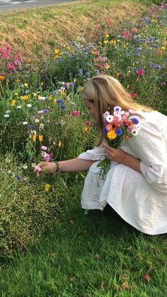 a woman kneeling down in the grass picking flowers