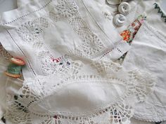 several different types of sewing and thread on a tablecloth with lace, buttons, and spools of thread