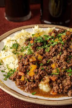 a white plate topped with mashed potatoes covered in ground beef and veggies