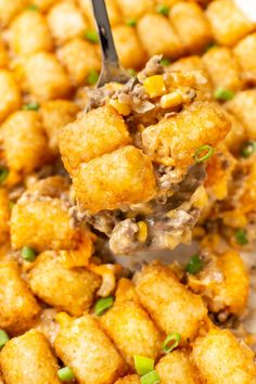 a spoon full of tater tots on top of a white plate with green onions