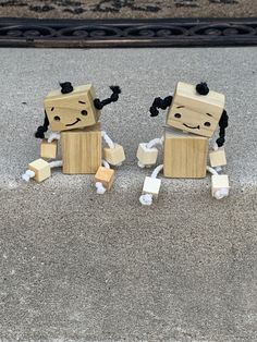 two wooden toy figures made to look like they are sitting on the ground next to each other