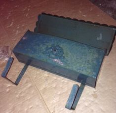 an old blue box sitting on top of a floor next to two pieces of metal