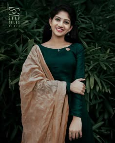 a woman standing in front of some plants wearing a green dress and brown shawl