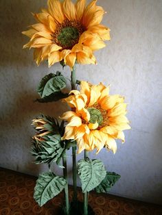 three yellow sunflowers are in a vase on the floor next to a wall