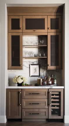 a kitchen with wooden cabinets and marble counter tops, wine glasses on the cabinet doors