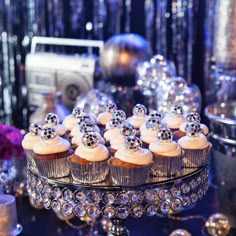 cupcakes with white frosting and silver decorations on a glass cake platter