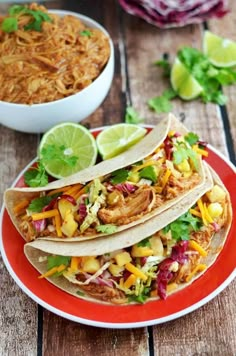 three tacos on a red plate next to a bowl of chili and limes