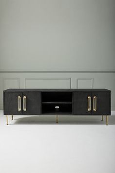 a black and gold tv stand with two doors on each side, in front of a white wall