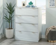 a white chest of drawers sitting next to a potted plant