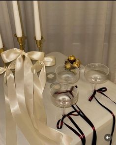 a table topped with candles and glasses filled with liquid next to ribbon tied around the candle holders