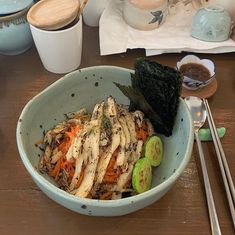 a bowl filled with food next to chopsticks and two cups of coffee on a table