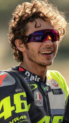 a close up of a person wearing sunglasses and a motorcycle outfit with long curly hair