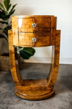 a small wooden table with two drawers on it's sides and a plant in the background