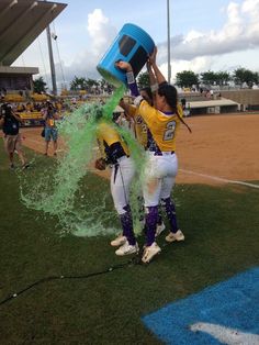 two baseball players are spraying water on each other with buckets at the end of the field