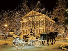 two horses pulling a carriage with people in it down the street at night time,