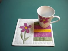 a coffee cup sitting on top of a table next to a patchwork place mat