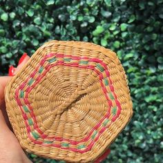 a hand holding a small woven basket in front of a green bush with red, pink and green trim