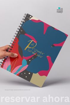 a hand is holding a spiral notebook with the cover open and it's colorful design