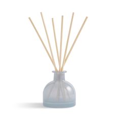 a blue glass vase filled with reeds on top of a white table next to a wooden stick