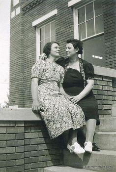 two women are sitting on the steps near a brick building and one is holding her head