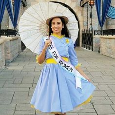 a woman in a blue dress is holding an umbrella and smiling at the camera while standing on a brick walkway