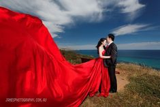 a man and woman standing next to each other on top of a hill near the ocean