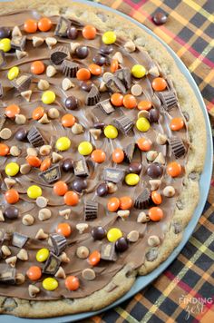 a cookie with chocolate and candy toppings is on a plaid tablecloth, ready to be eaten