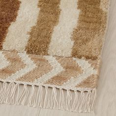 a brown and white rug with fringes on top of wooden floor next to wall