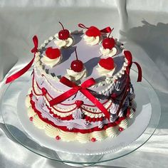 a white cake with cherries and ribbons on a glass platter, ready to be eaten