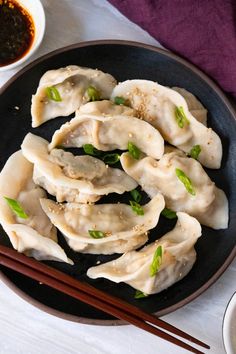 some dumplings are on a black plate with chopsticks