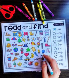 a hand holding a marker next to a worksheet on a table with crayons and markers