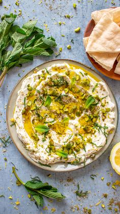 a bowl of hummus with olives, herbs and pita chips on the side