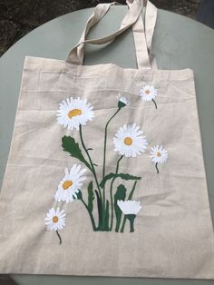 a tote bag with daisies painted on it sitting on top of a table