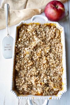 an apple and oatmeal dessert in a white dish next to two spoons