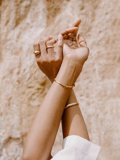 a woman with her arm wrapped around another person's wrist and wearing two gold bracelets