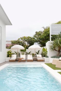 an outdoor pool with lounge chairs and umbrellas next to the swimming pool is surrounded by greenery