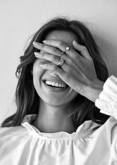 a woman smiling and covering her eyes with her hands while wearing a white blouse, black and white photo