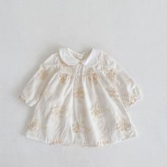 a white dress with gold flowers on it and a collared neckline, sitting on a white surface