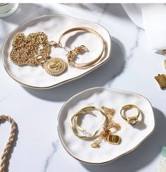 two white plates with gold jewelry on them sitting on a marble counter top next to other accessories