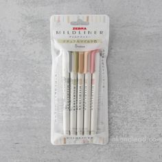 four different colored markers in a package on a gray surface with the words milliner next to it