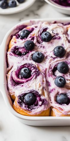 blueberry rolls with cream cheese frosting in a white casserole dish on a marble surface