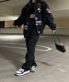 a woman in black jacket and white sneakers walking across an empty parking lot with her handbag