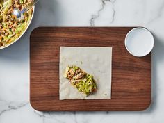 a wooden cutting board topped with food next to a bowl