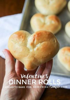 someone is holding a heart shaped bread roll in front of some rolls on a baking sheet