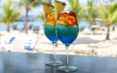 two glasses filled with colorful drinks sitting on top of a table next to each other