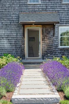 a house with lavender flowers in front of it and a stone walkway leading to the door