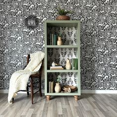 a green book shelf with books on it in front of a wallpapered background